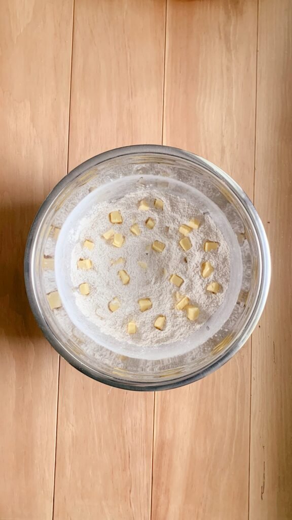 a stainless steel bowl of dry ingredients and cubed butter for fresh milled white chocolate strawberry scones on a wooden table
