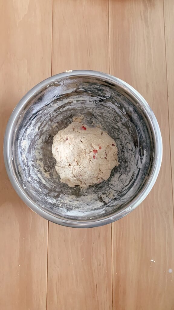 a stainless steel bowl of dough for fresh milled white chocolate strawberry scones on a wooden table