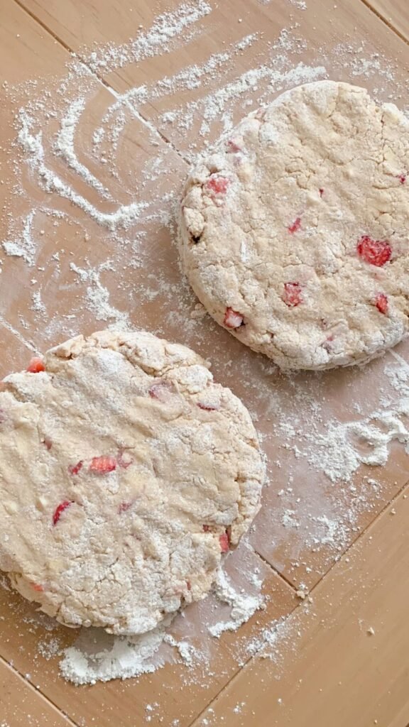 two 1" thick disks of fresh milled white chocolate strawberry scone dough on a lightly floured surface on a wooden table