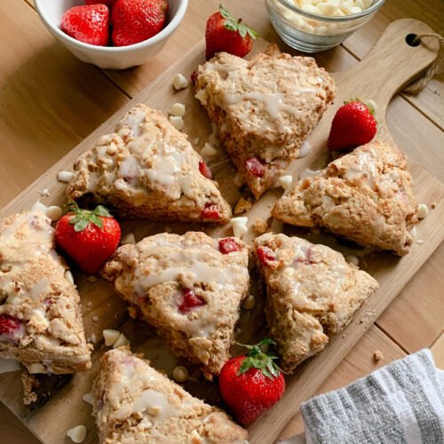 fresh milled white chocolate strawberry scones arranged on a wooden cutting board with strawberries and white chocolate on a wooden table